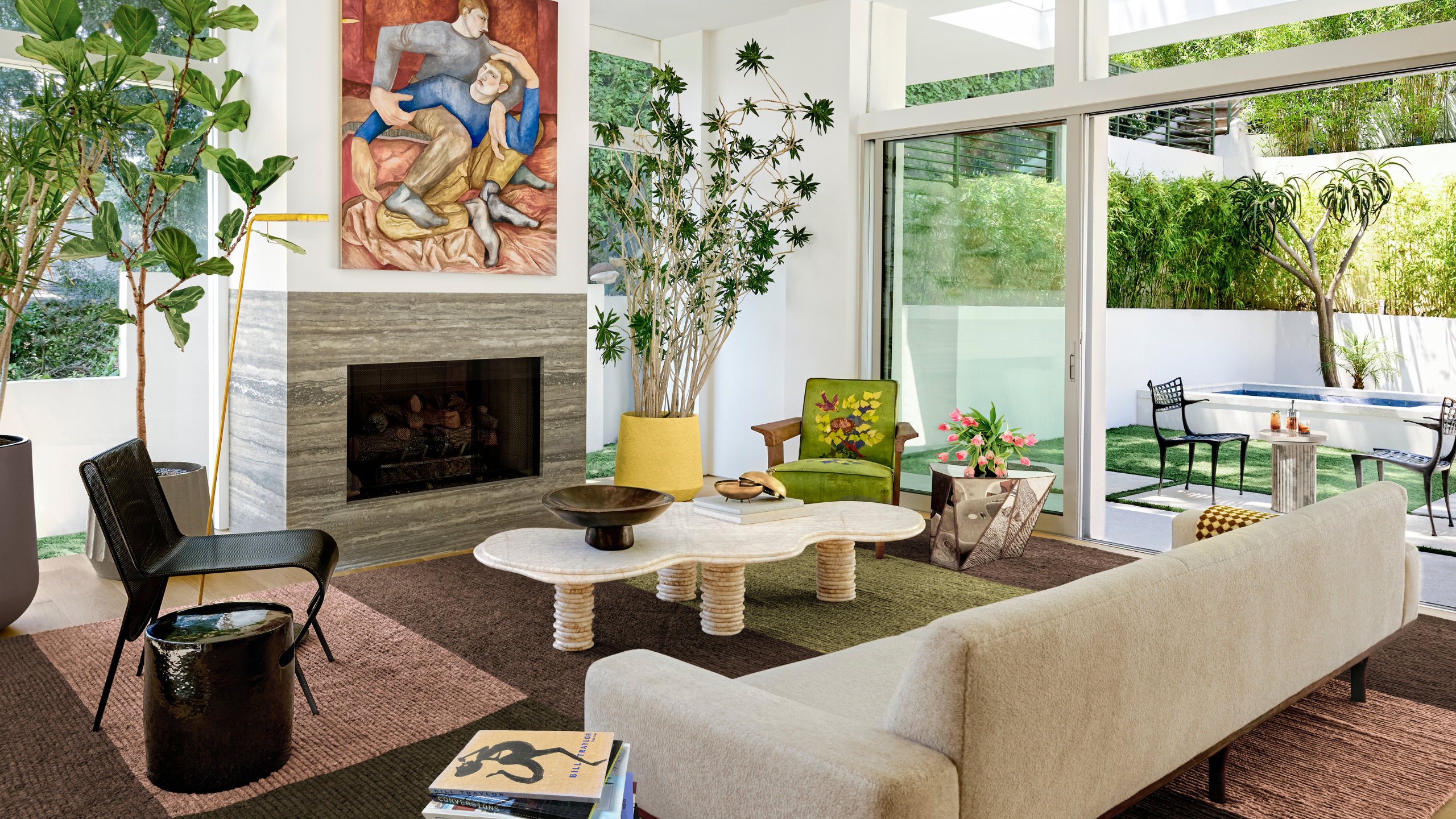 Layered, contemporary living room featuring colorful artwork, faded terracotta rugs, a low-slung cream sofa, and a sculptural irregularly shaped coffee table topped with a pedestal bowl.