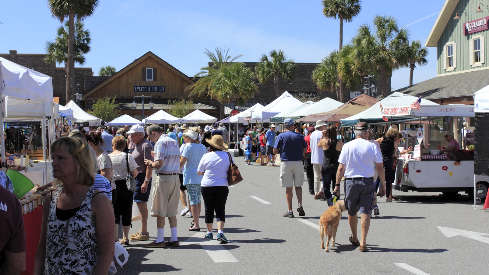 The Villages, FL, USA - April 1, 2017: Street market shops under canopies sell to shoppers on a sunny day. People at the Farmers&#039; market shops near Paddock Square.