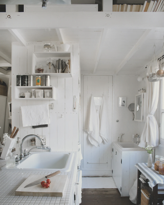 A small white kitchen with a laundry/utility area with modular shelving