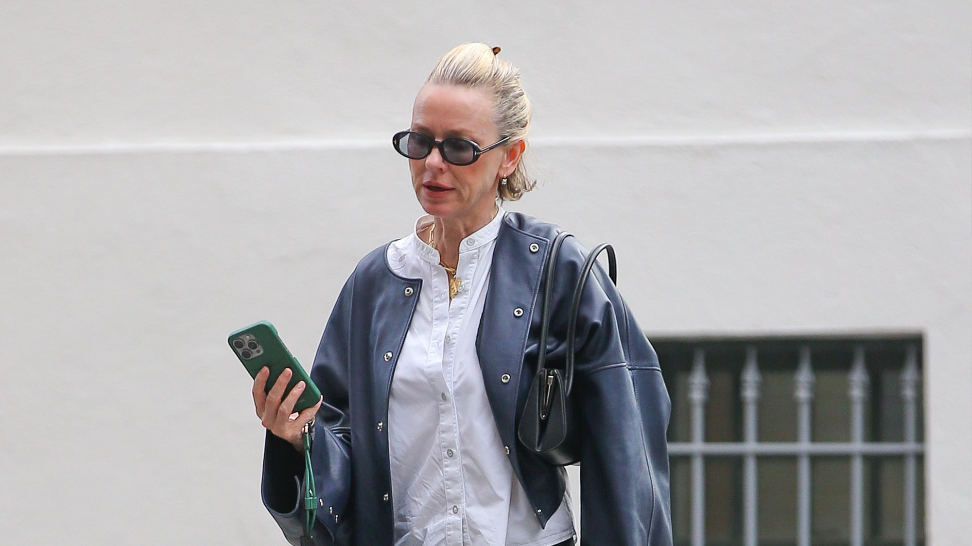 Naomi Watts wearing a white button-down, black leather jacket, black jeans, and white jazz shoes