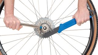 A pair of hands holding a chain whip and lockring tool in place on a bike wheel