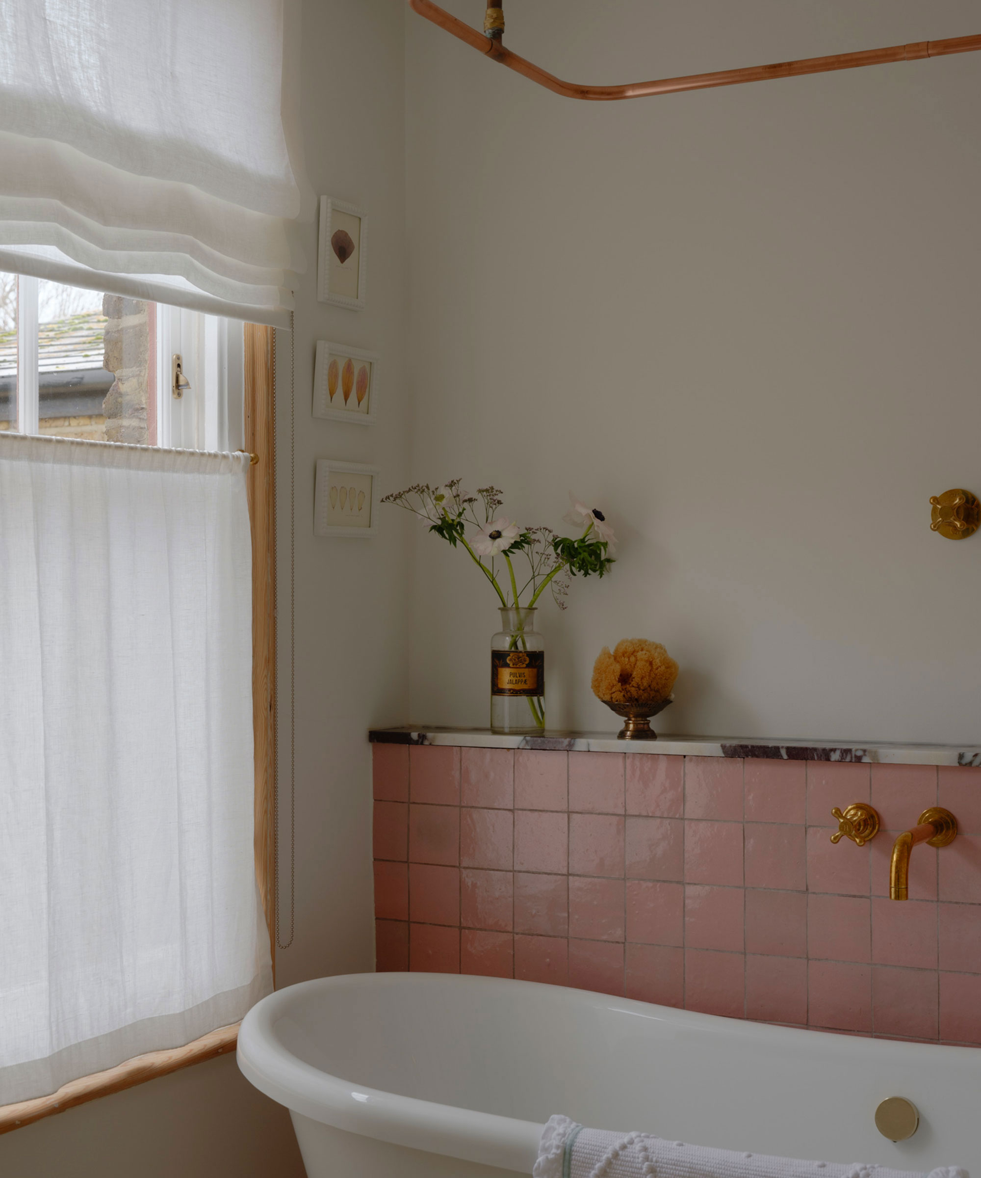 small bathroom with pink tiles with rolltop bath and window with net curtains