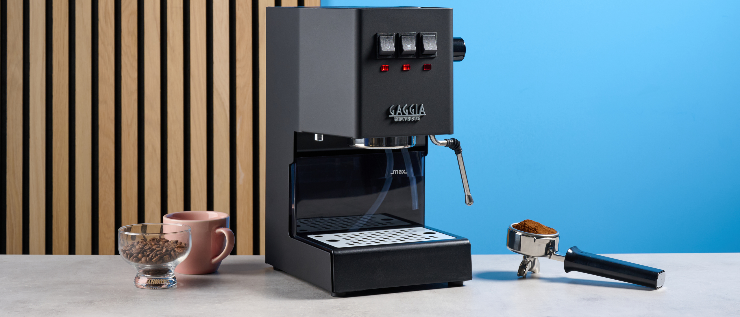 The Gaggia Classic E24 Evo Pro with accessories against a blue background and on a stone surface