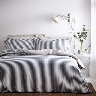 A blakc and white striped bedlinen set on a bed in a white bedroom with a vase of flowers on the bedside table