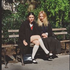 forever magazine founders nat ruiz and anika jade levy pose on a new york city park bench wearing black peacoats and white socks with mary janes or a long black skirt