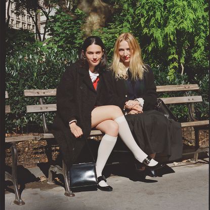 forever magazine founders nat ruiz and anika jade levy pose on a new york city park bench wearing black peacoats and white socks with mary janes or a long black skirt