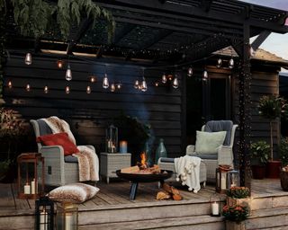 A covered decking area with fairy lights and chairs round a firepit