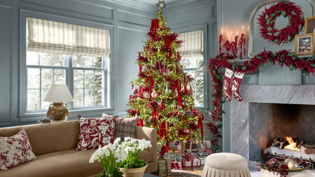 Opulently decorated Christmas tree dressed in plumes of burgundy amaranthus, tassels, and mercury glass, inside of a sky-blue-living room filled with wrapped presents and antique-inspired accents