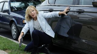 Kelli Giddish as Detective Amanda Rollins hiding behind a car in Law & Order crossover event