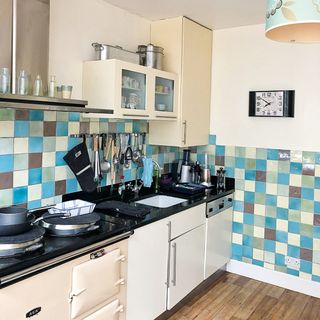 A cream kitchen with Aga oven and multicoloured tiled splashback with green, brown, blue and taupe square tile decor