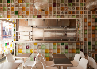 A restaurant with simple decor, except the back wall is covered in pastel colored glass blocks