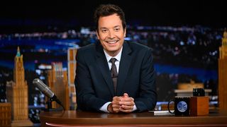 Jimmy Fallon smiles while sitting at The Tonight Show desk during a July 2026 episode. He's in a suit and tie.
