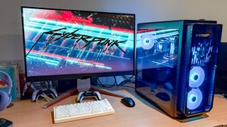 Acer Predator Orion 7000 on desk with monitor, keyboard, mouse and PS5 controller next to it with Cyberpunk 2077 in action