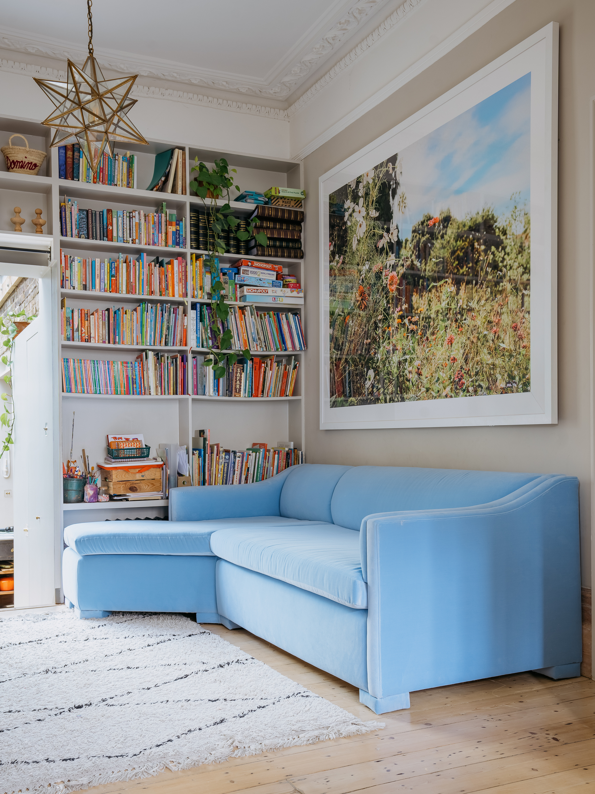 Jodie Hazlewood of The House Upstairs' designed living room with a low-back baby blue sofa in the corner of a room with modern art on the walls and book shelves