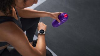 person looking at their Garmin running watch checking their hydration reminder while holding a water bottle in their other hand