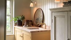 A yellow painted vanity unit with a wooden top. Two brass taps, and an inset sink