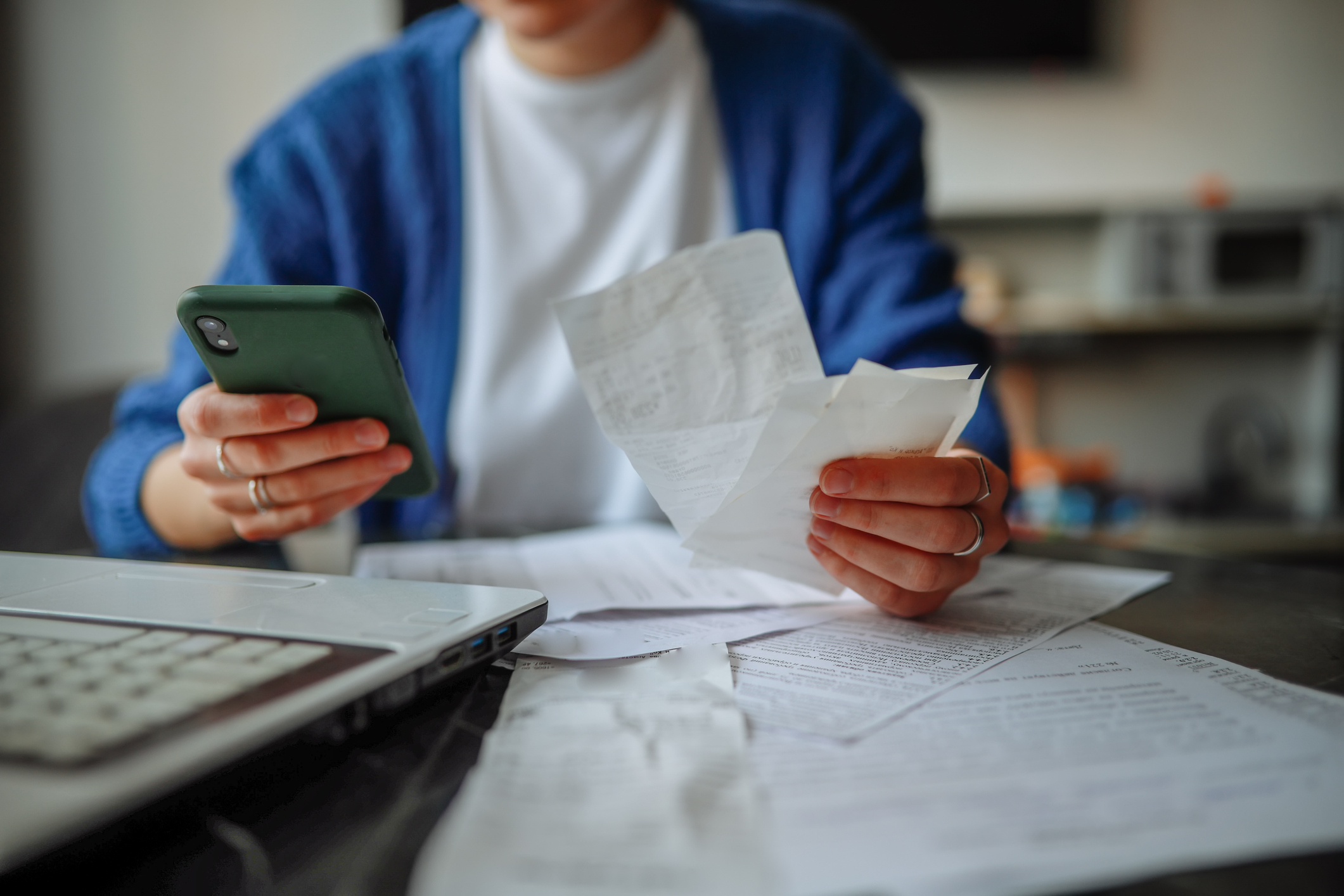 Woman sitting behind a laptop, smartphone, and papers at a table at home