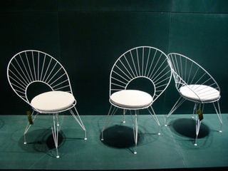 Three white outdoor chairs photographed on green surface against a green wall