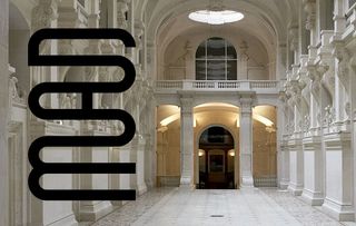 The main hall of a museum features classical decor including tall ceilings, pillars, glass windows, and warm light. On the left-end side of the image, a sign reads "MAD" in black, vertical characters.