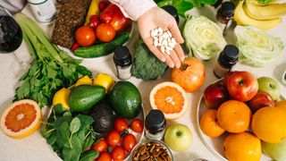 A selection of vitamin and nutrient-rich foods, including oranges, leafy green vegetables, avocado, tomatoes and nuts