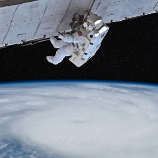 astronaut holding a long structure over cloudy Earth