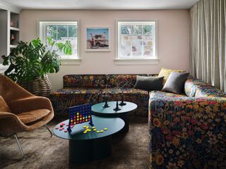 Playroom with pale pink walls, dark floral patterned oversized corner sofa, black nesting coffee tables and brown armchair