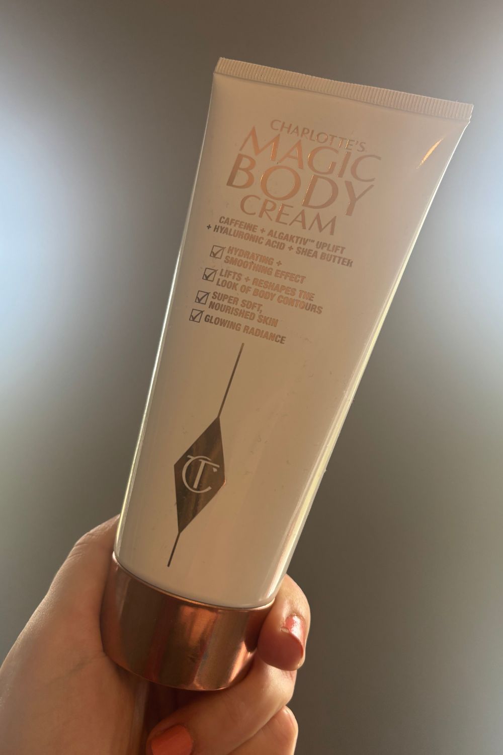 A HAND HOLDING A TUBE OF CHARLOTTE TILBURY MAGIC BODY CREAM
