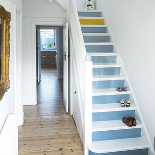 A white hallway with wooden flooring and painted blue and yellow stairs