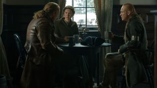 Jamie Fraser, Claire Fraser and Young Ian sit at an inn table in Outlander season 7