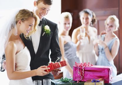 A wedding couple are receiving gifts at a party. The gift is in red packaging. 