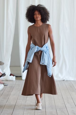 a model wears a brown dress with a denim jacket tied around her waist