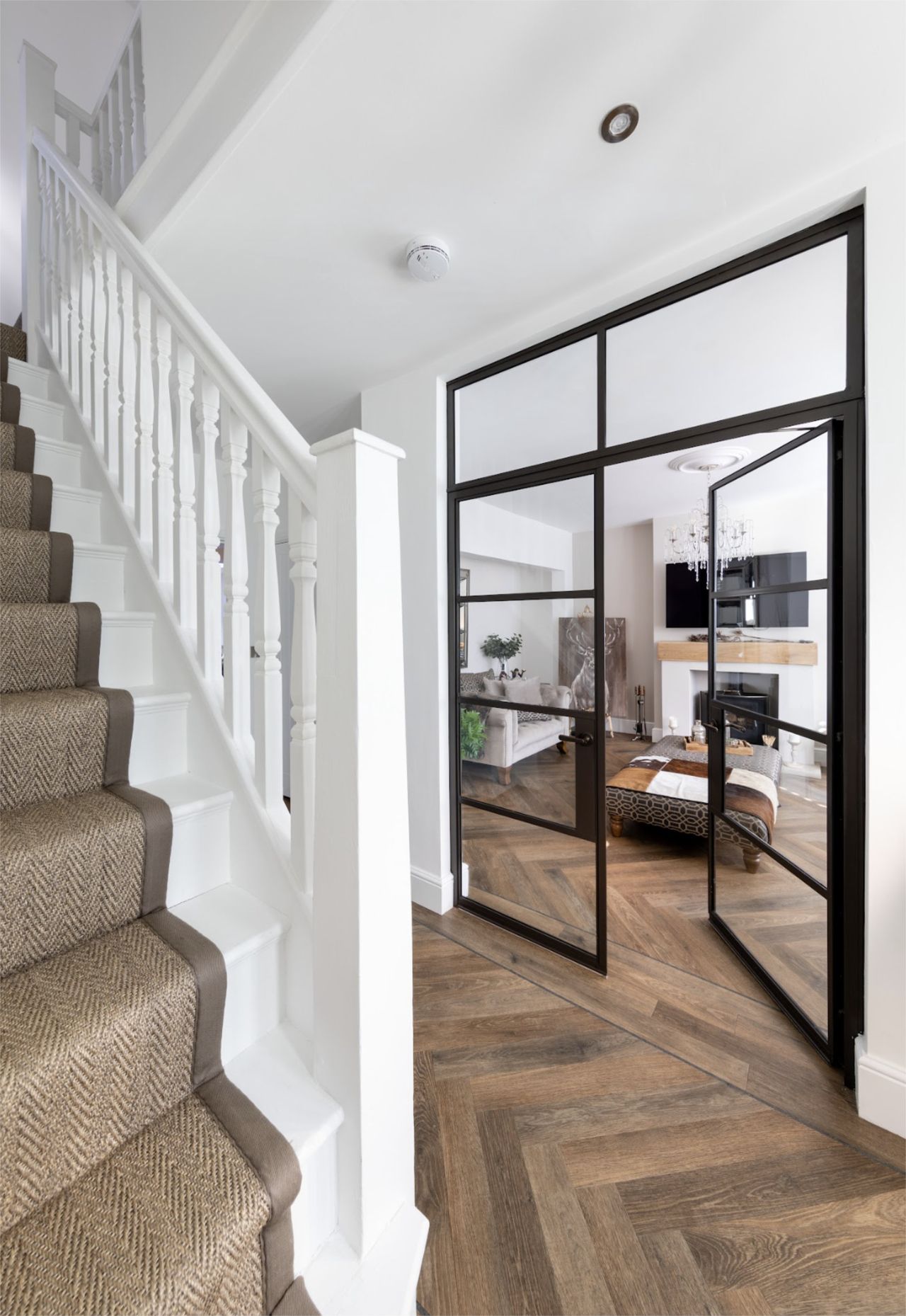 A hallway and staircase with parquet floors and critall-style doors leading to a living room
