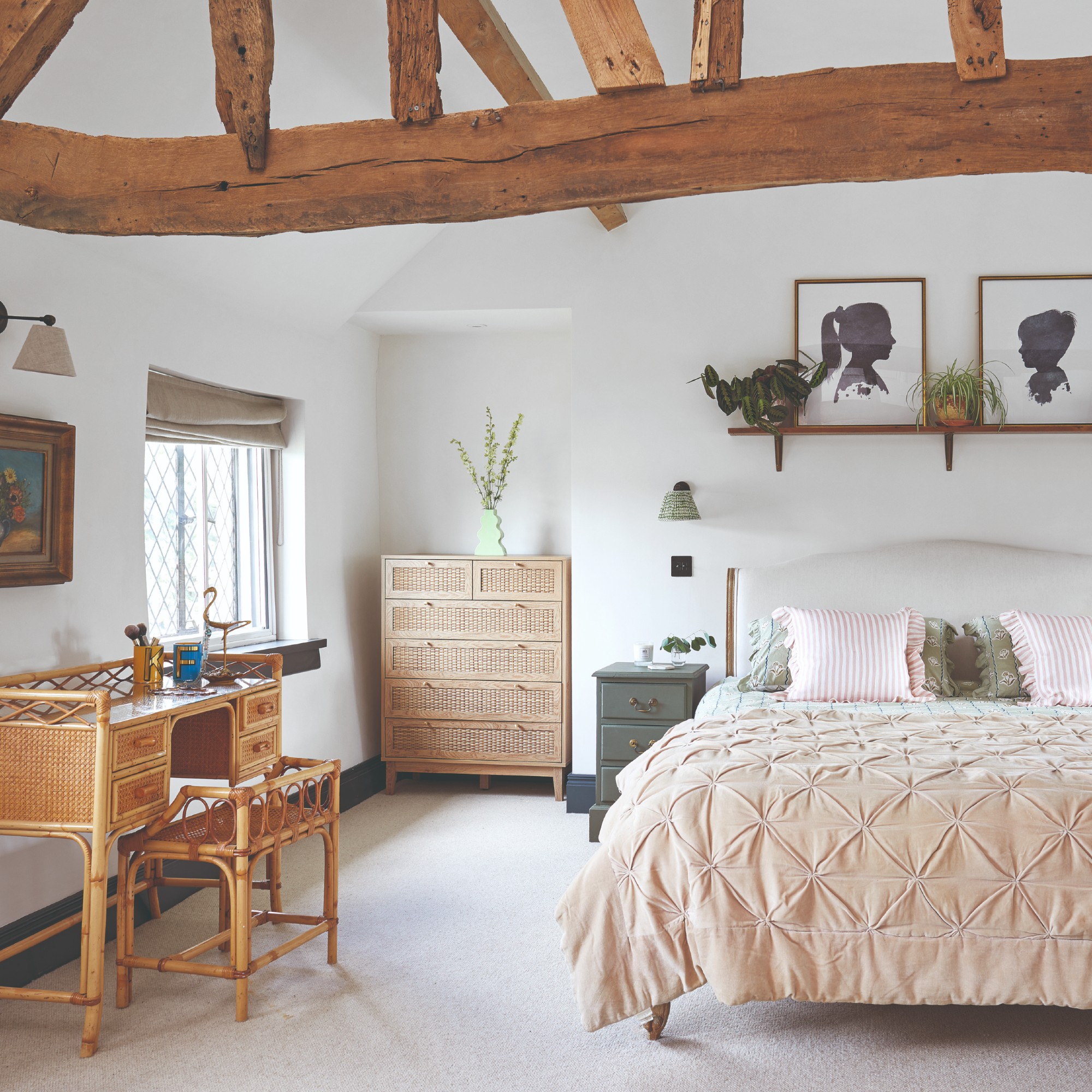 A white bedroom with exposed warm wood beams, a wooden chest of drawers and a bamboo desk with a matching stool