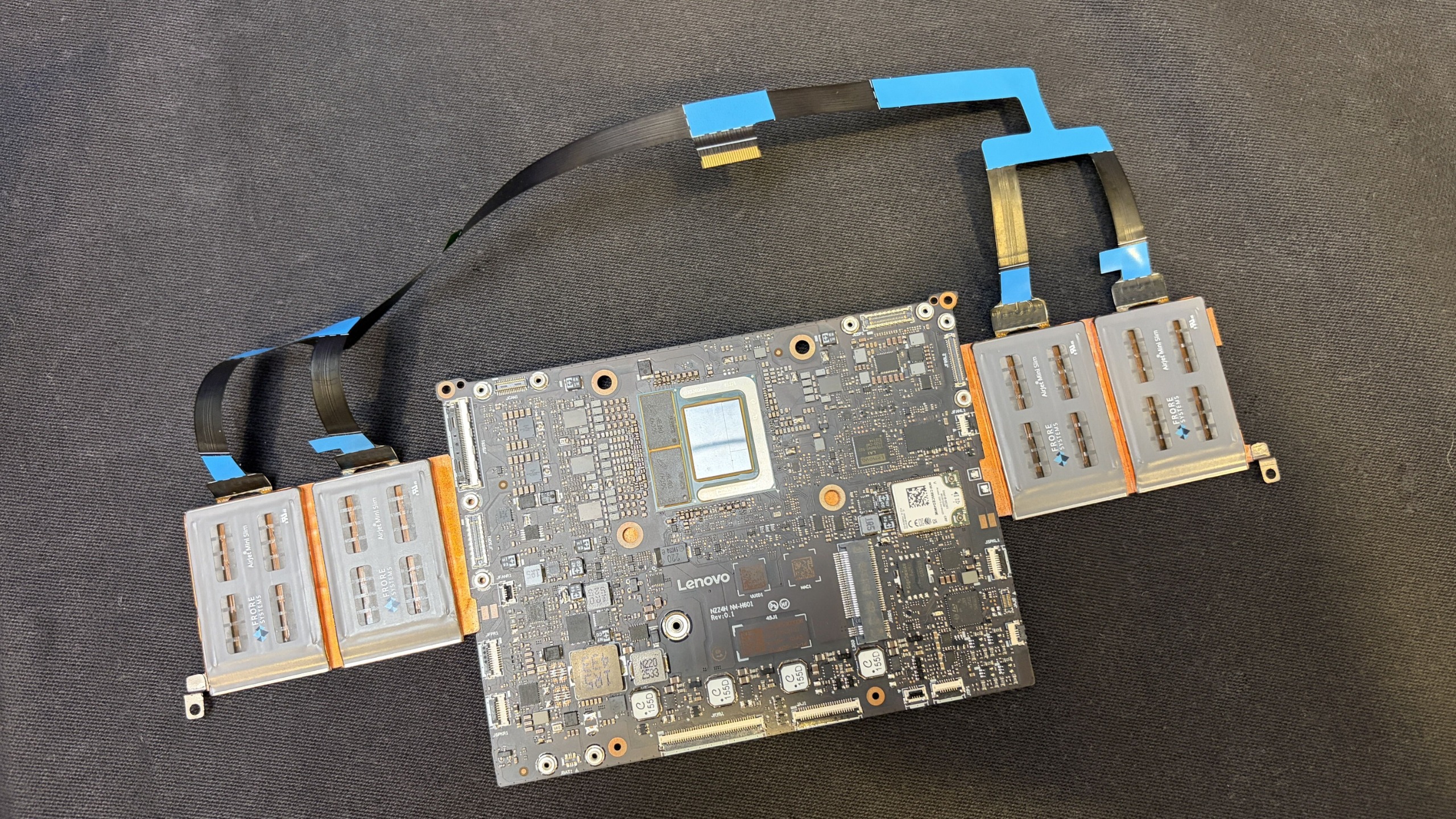 Disassembled Project Aeroblade motherboard with attached ribbon cables and side connector modules, displayed on dark fabric in a technical, instructional setting.