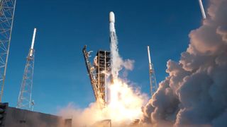 a white and black rocket lifts off into a bright blue sky leaving a large white plume in its wake