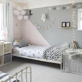 Grey and pink kids room with wrought iron twin beds and fairy lights