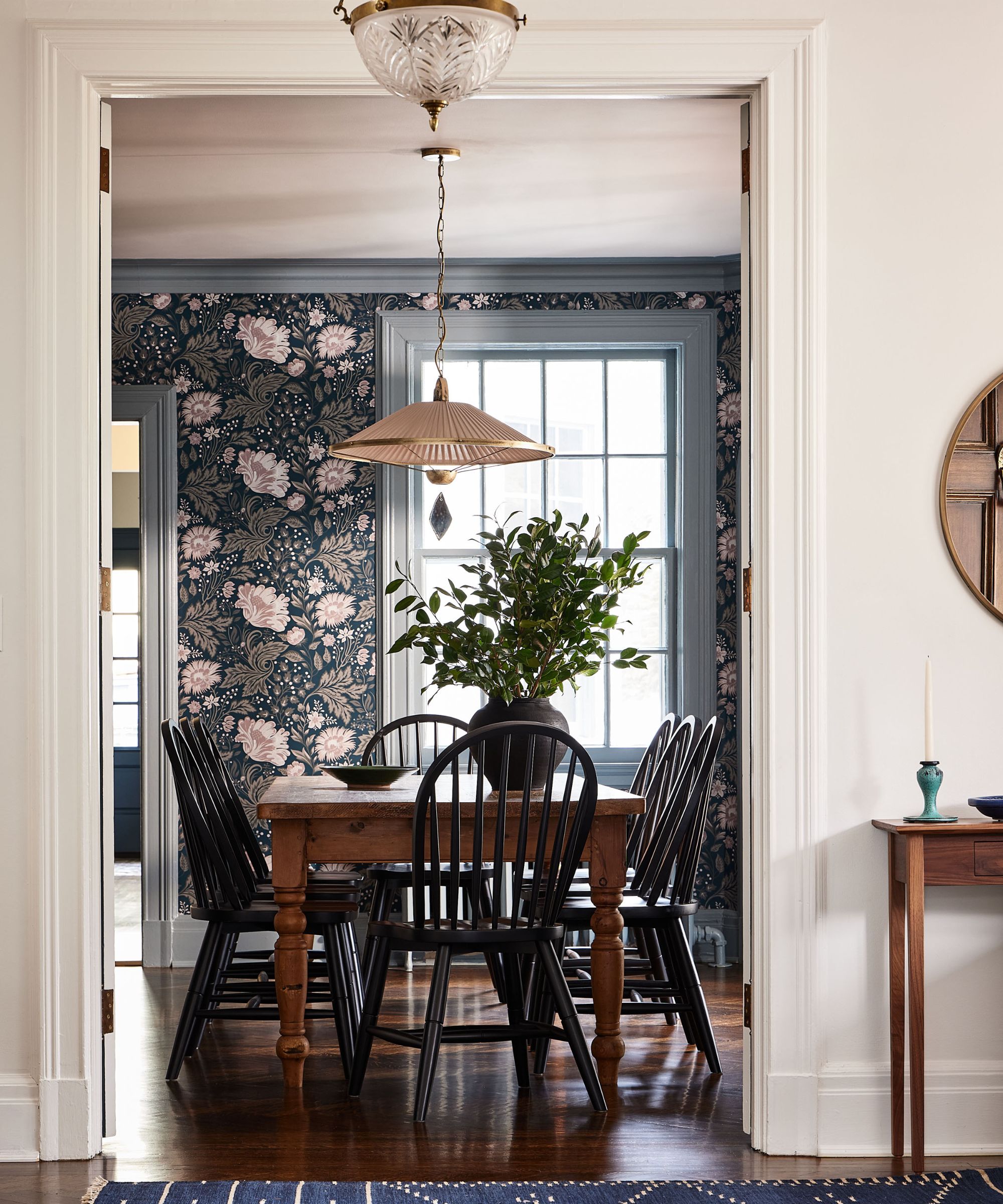 Hallway looking into dining room with floral wallpaper, wood dining table and chairs and pendant light