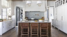 A kitchen with white cabinets, a wooden island with a white countertop, and three bar stools with woven backrests