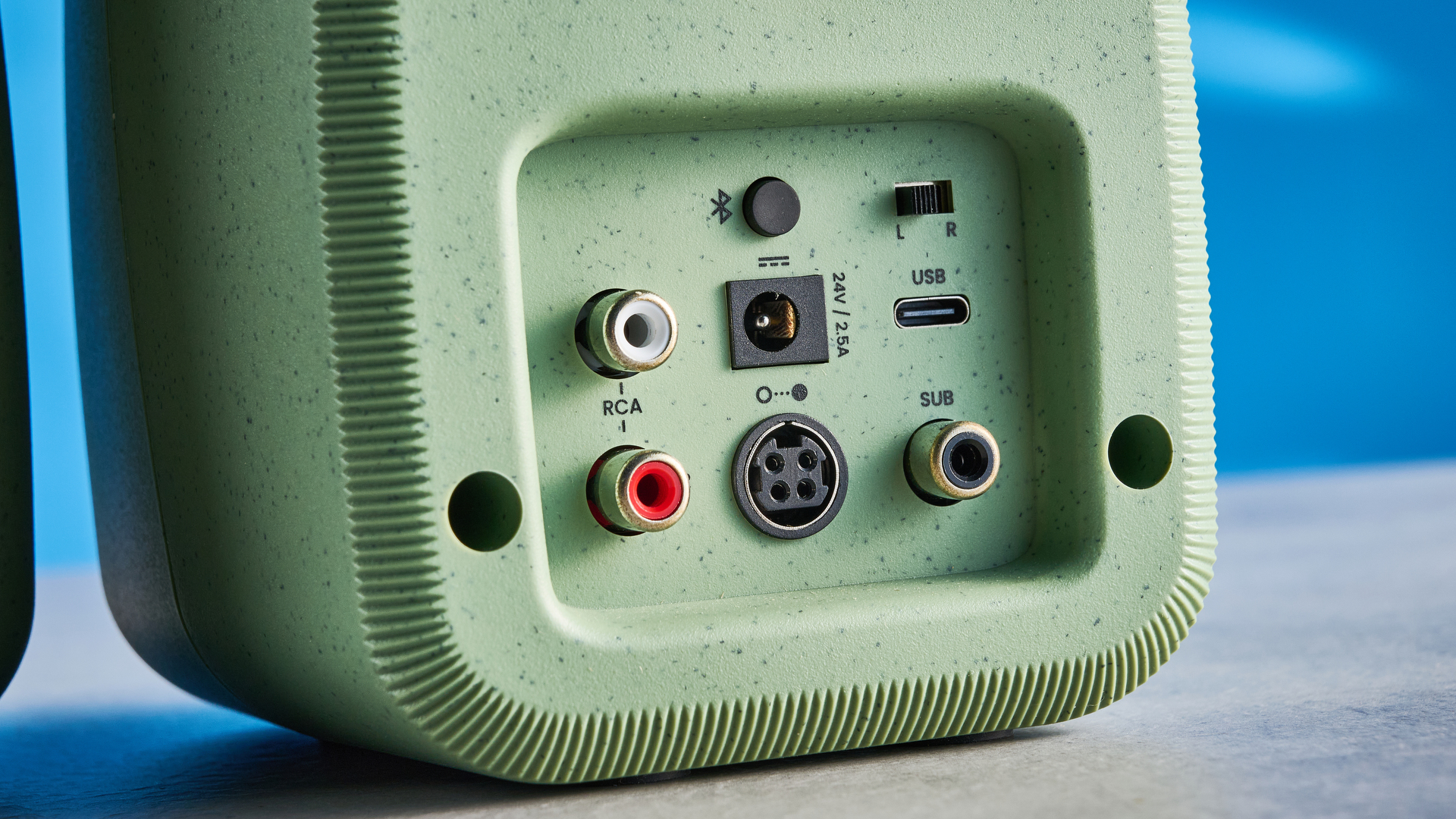 Kanto UKI bookshelf speakers in sage photographed in front of a blue background