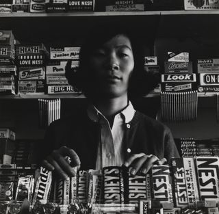 Black and white photograph of woman behind sweets counter