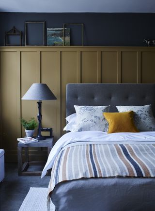 bedroom with grey and mustard color scheme, upholstered bedhead, panelling, side table, artwork, stripe blanket