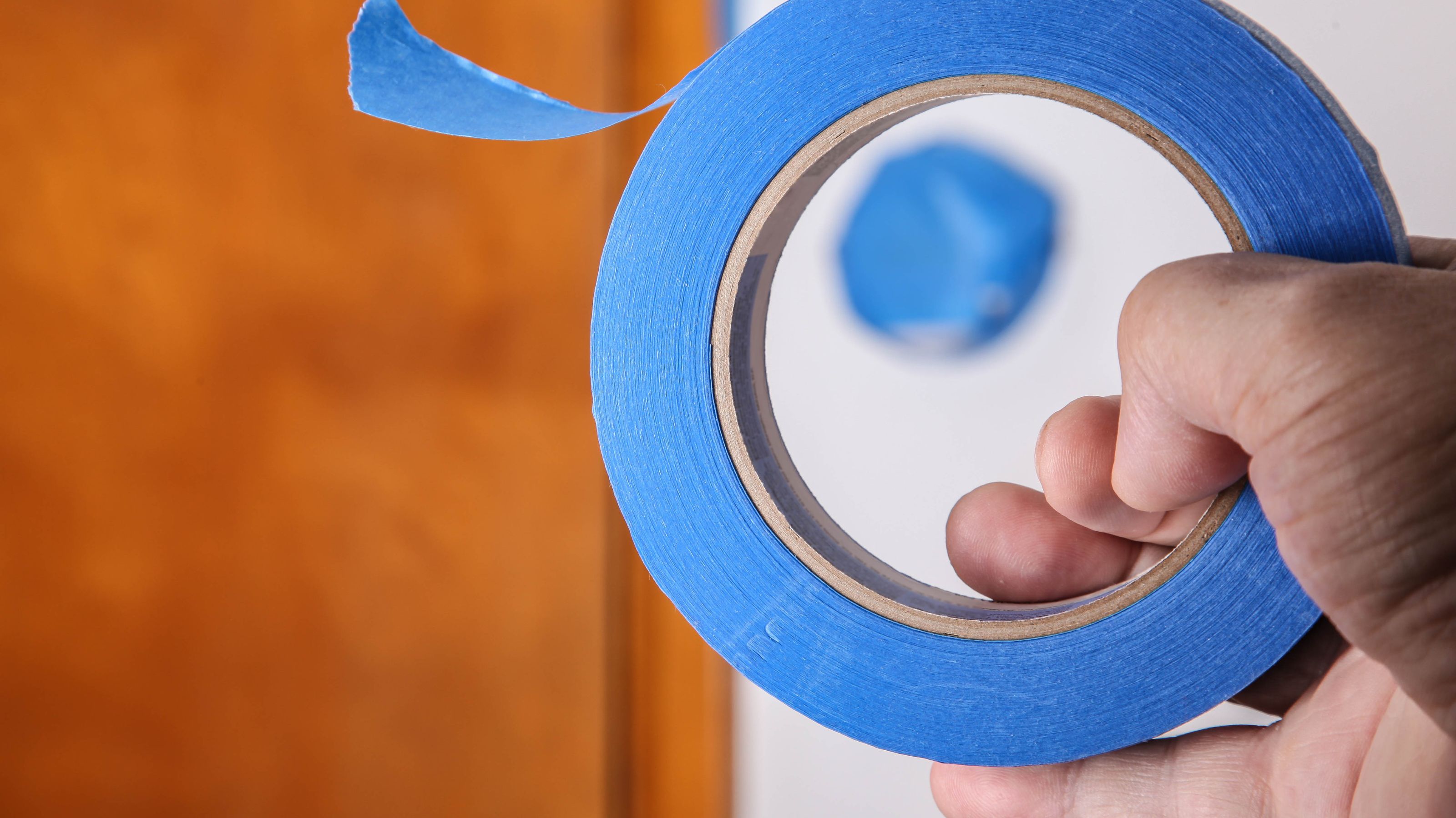 Hand holding blue masking tape in front of a plain wall and varnished door