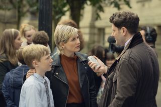 Toby Eden, Jodie Whittaker, and Matthew James Hinchliffe as a son and mother being interviewed by a reporter on a street in the show toxic town