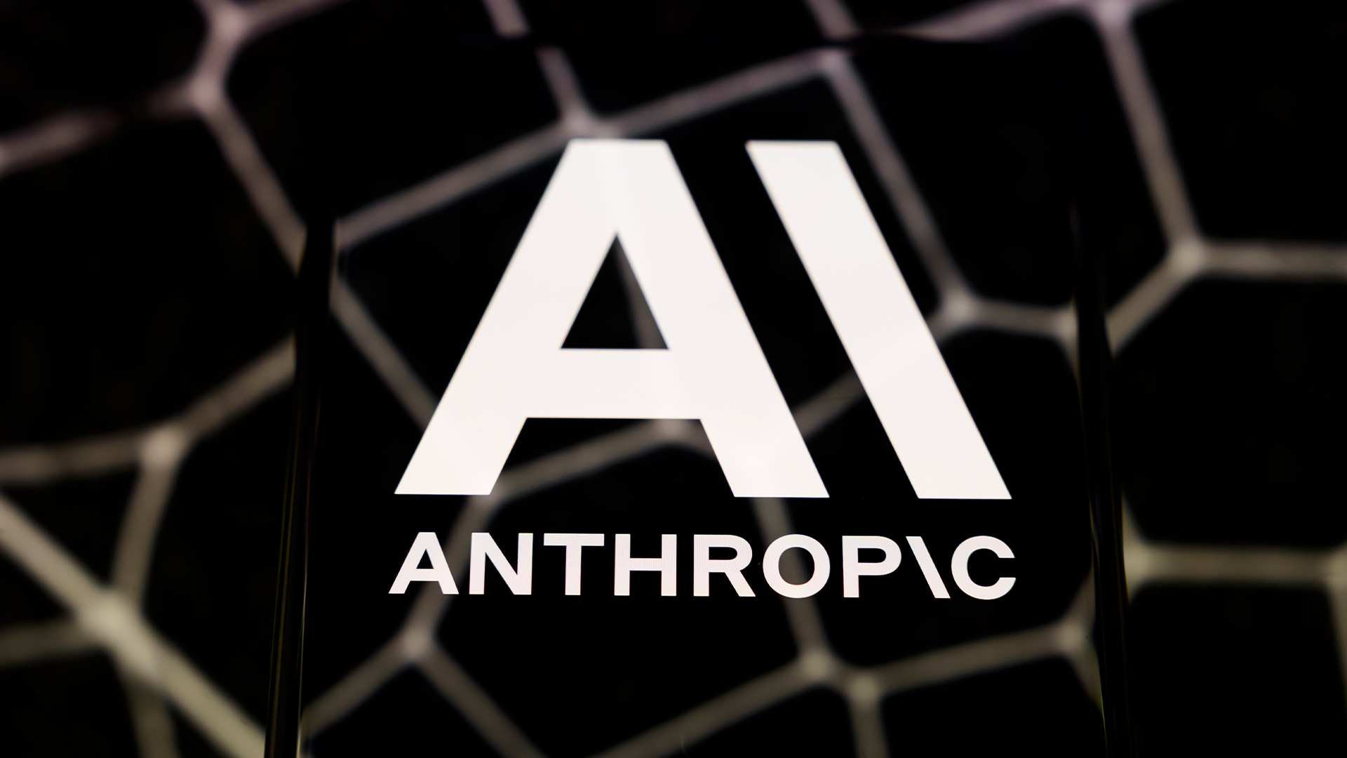 Anthropic logo and branding pictured on a smartphone screen placed on a reflective surface.