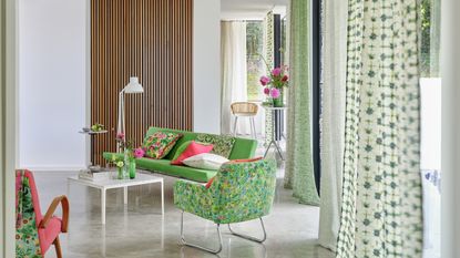 A decluttered and organised living room with a green couch, chair and floaty floor to ceiling green curtains