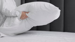 Someone holding a pillow over a bed and fluffing it