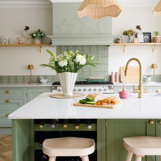 green kitchen island with white surface, in front of kitchen cabinets and patterned splashback