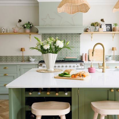 green kitchen island with white surface, in front of kitchen cabinets and patterned splashback