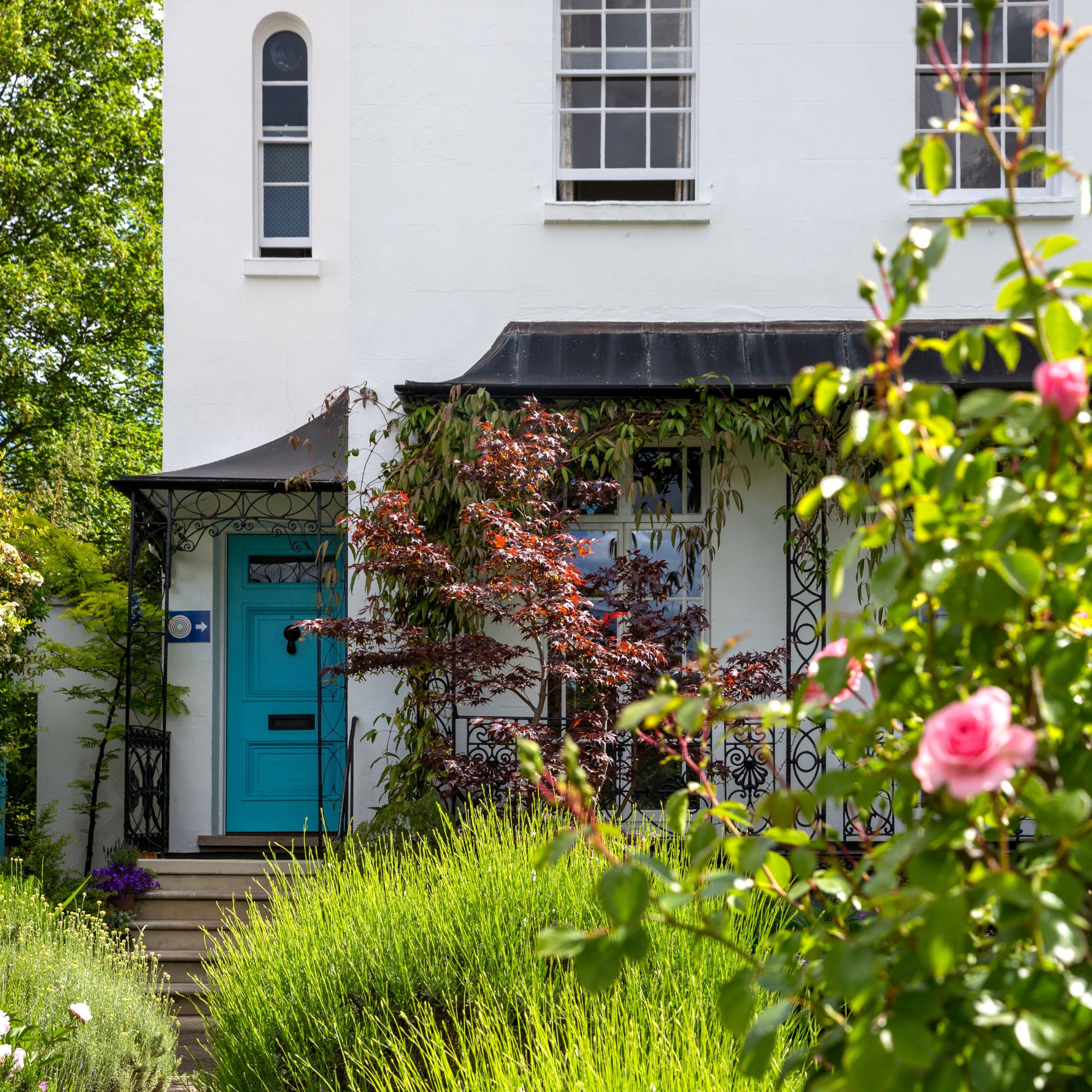Front of a period property painted white with a blue front door , and an established front garden