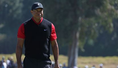 Tiger Woods strolls up the fairway in a red top and black jumper
